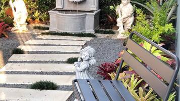 A garden with a stone fountain, statues, and a bench.