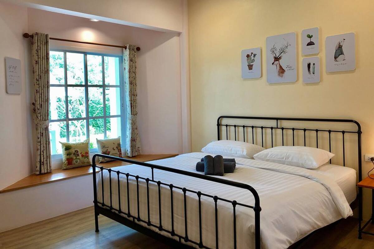 A bedroom with a bed, a window with curtains, and wall art.