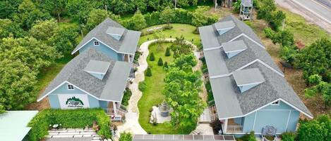 Una zona residencial con dos casas azules, un jardín central y una calle al fondo.