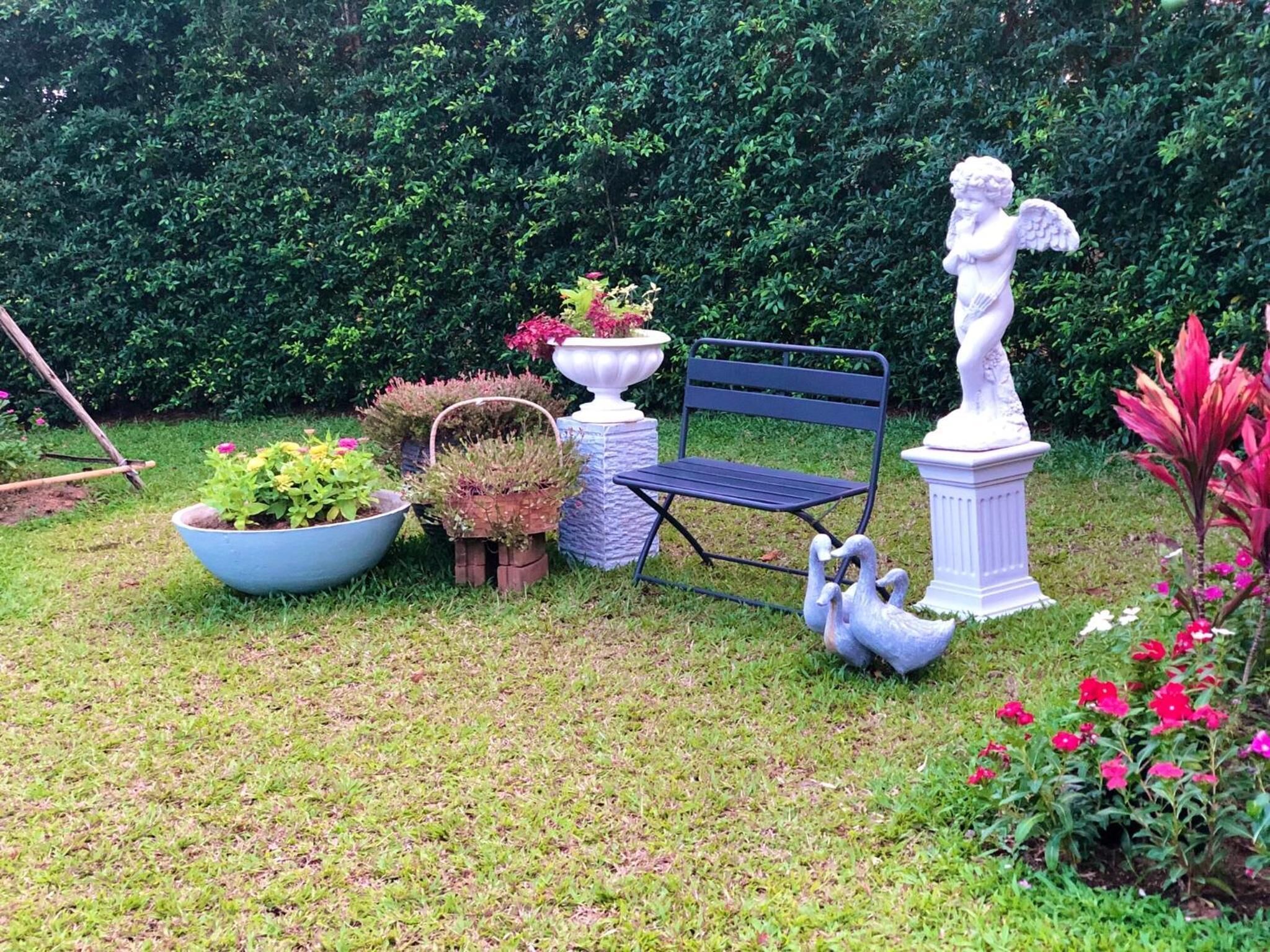 Un jardín con un banco, una estatua y diversas plantas en macetas.