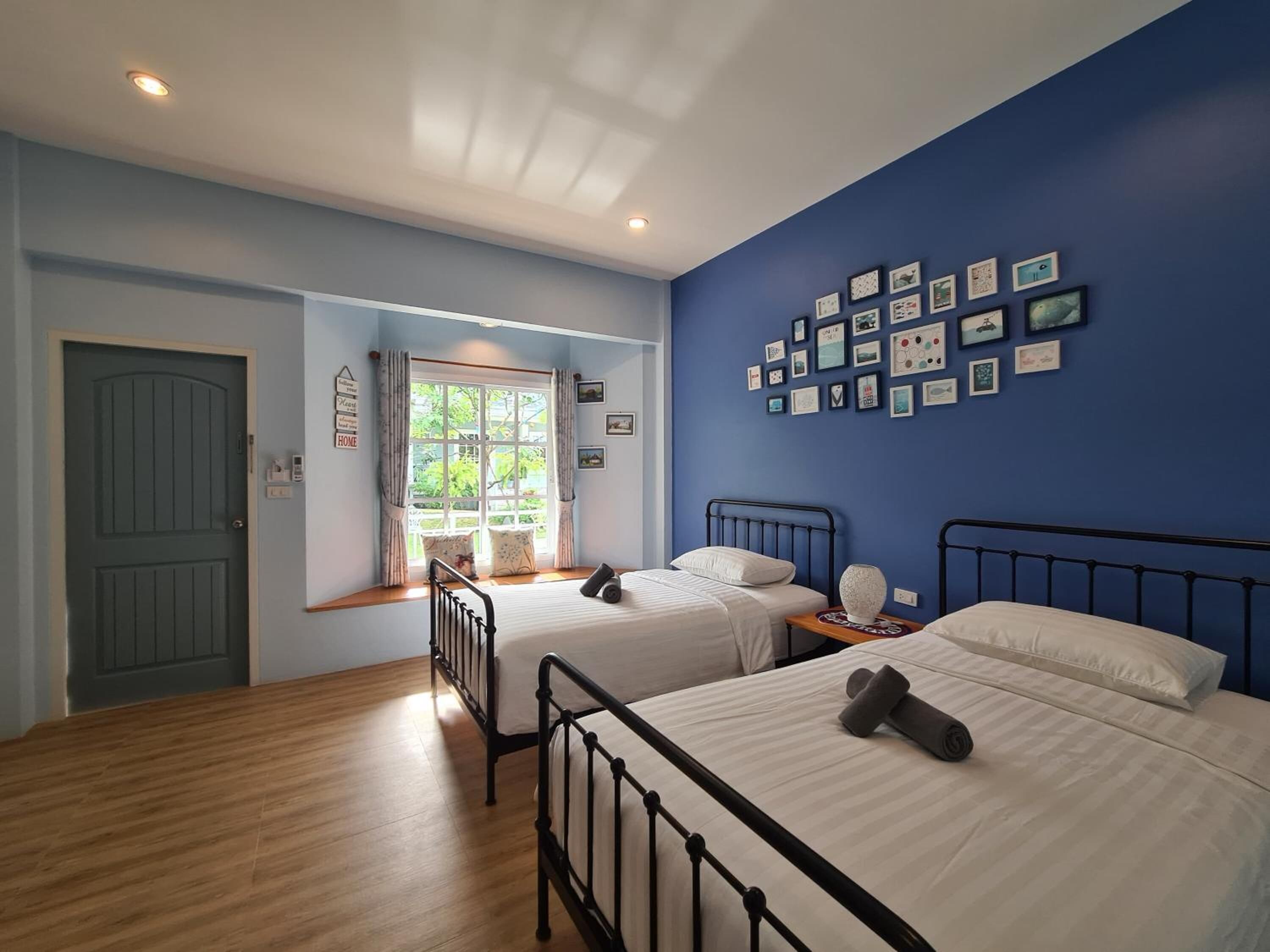 Une chambre avec deux lits, une fenêtre avec des rideaux, un mur orné de tableaux encadrés et une porte.