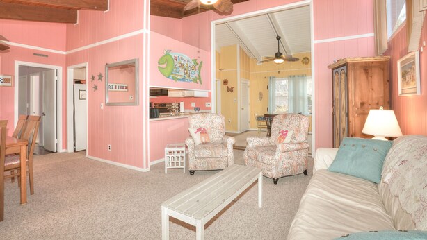 A pink-themed room with a dining area, two patterned armchairs, a sofa, a wooden bench, and a ceiling fan. - Come to the cottage! 3BR2BA - Bethany West. Pool, pickleball, tennis, gym. Pets! (Bethany Beach)