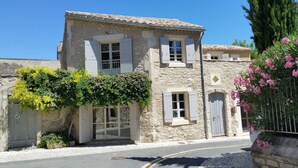 A stone building with a tiled roof, a small balcony, and a door with a metal gate. - Luxury Village House In The Heart Of Historic St.Remy-De-Provence (Saint-Rémy-De-Provence)