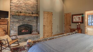 Une pièce chaleureuse avec une cheminée en pierre, des portes en bois, un lit et un téléviseur.