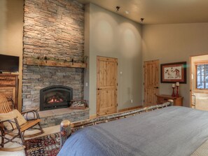 A cozy room with a stone fireplace, wooden doors, a bed, and a television.