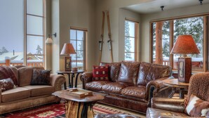 Un salon chaleureux, avec des meubles en cuir, une table basse en bois et de grandes fenêtres donnant sur un paysage enneigé.