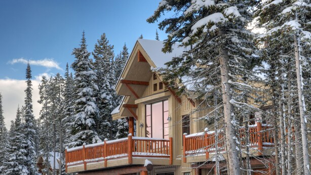 Un chalet en bois doté d’un balcon, entouré d’arbres couverts de neige.