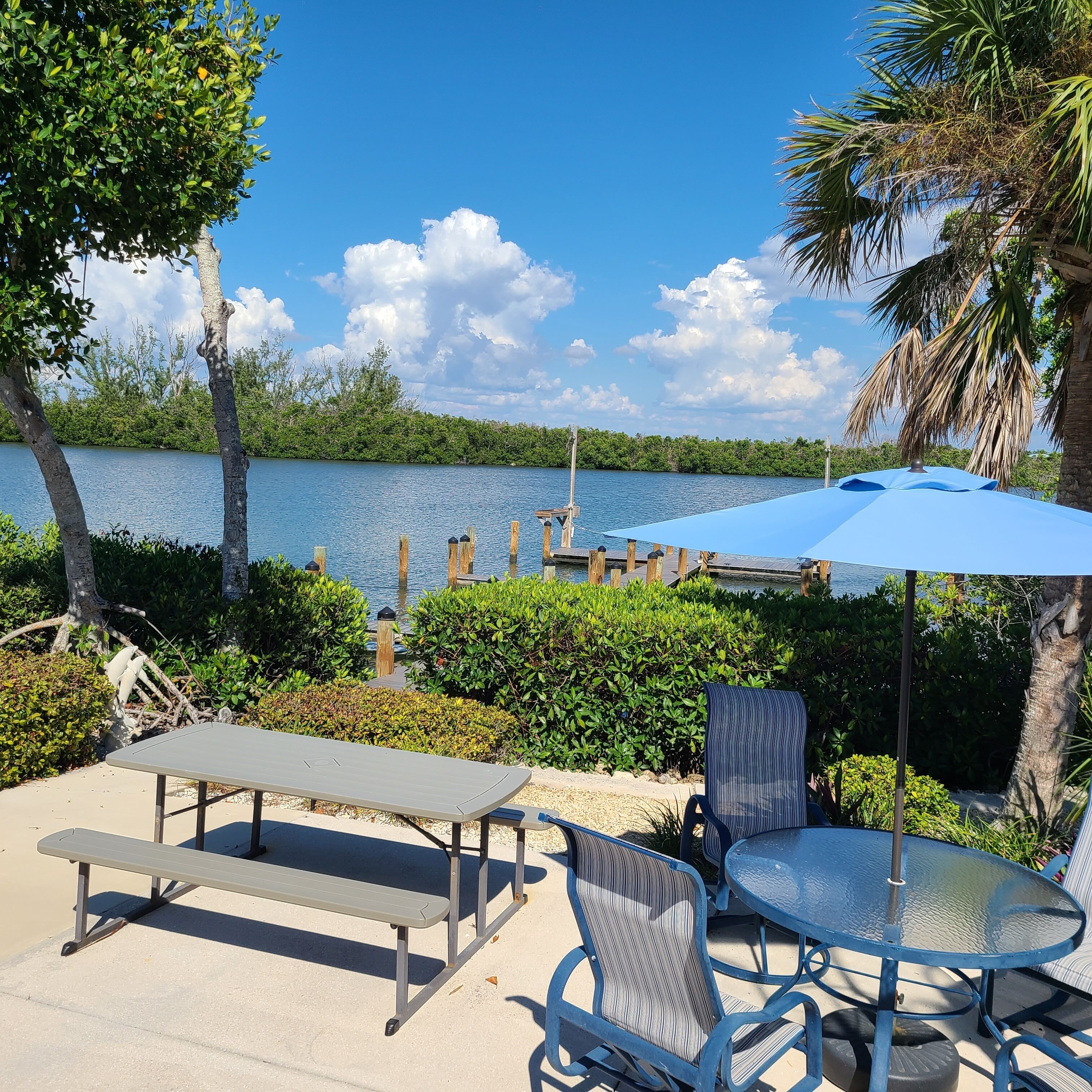 An outdoor patio with a table and chairs, a bench, and a view of a lake with a dock.