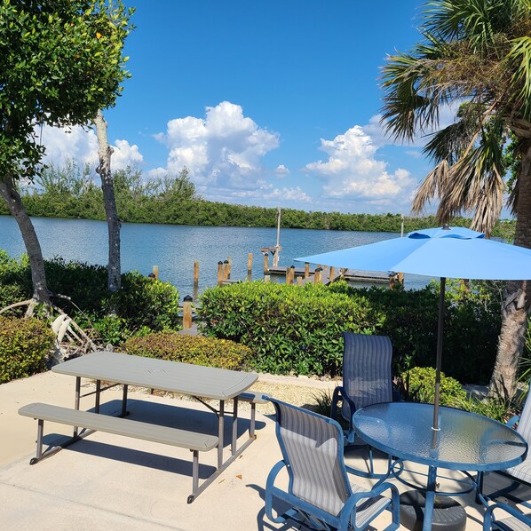 An outdoor patio with a table and chairs, a bench, and a view of a lake with a dock. - Very Nice, Clean Condo on Manasota Key! Close to Everything! (Englewood)