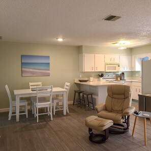 Un espace de vie compact comprenant un coin repas, une cuisine et un coin salon avec un fauteuil inclinable.