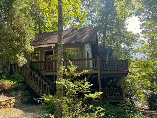 A two-story cabin with a wooden deck and stairs, surrounded by dense forest. - Hummingbird Hideaway - Lake Pets Hike Fish (Almond)