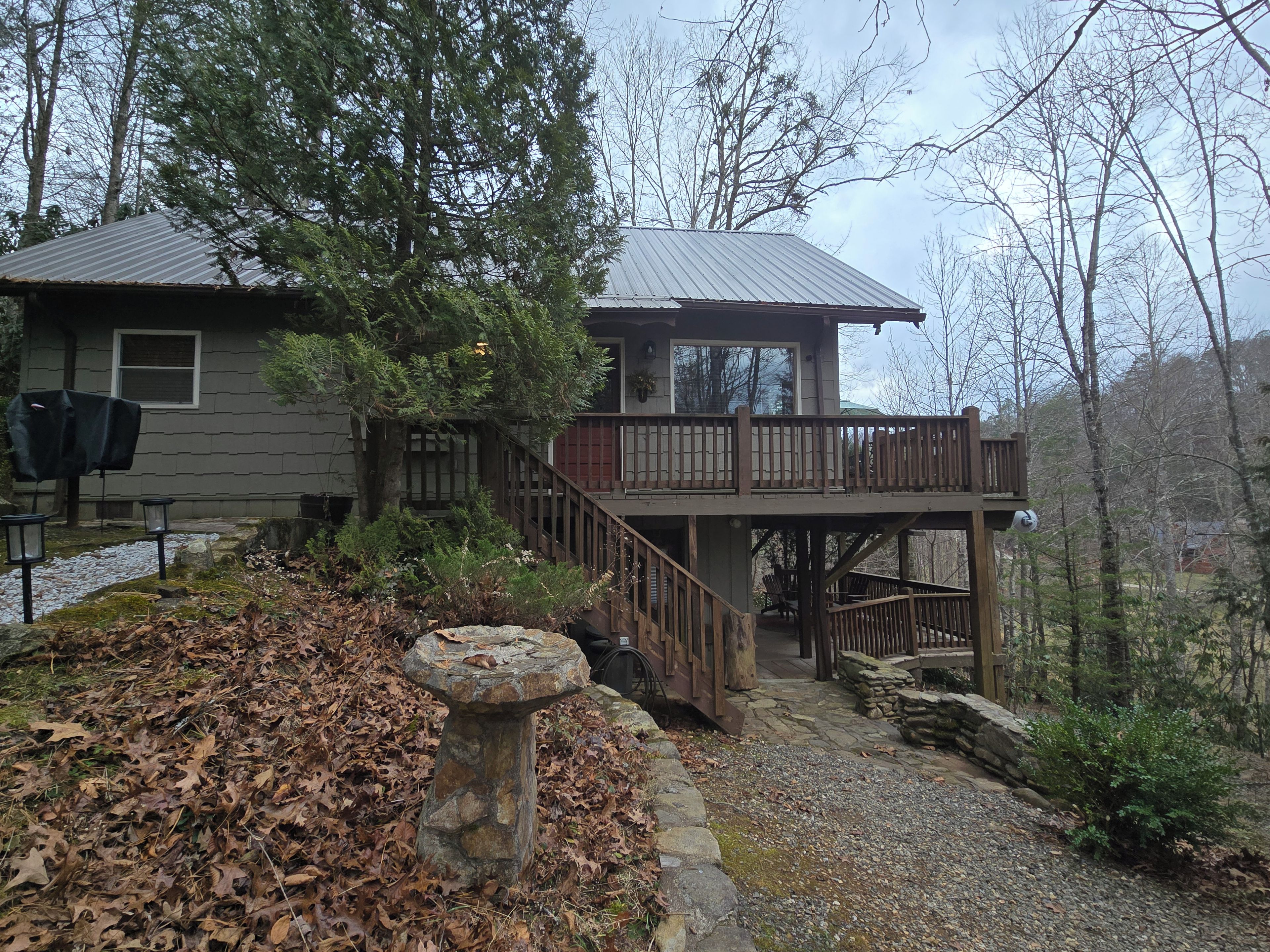 A two-story house with a deck, surrounded by trees and a stone pathway.