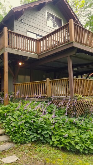 A wooden cabin with a balcony and a garden with purple flowers. - Hummingbird Hideaway - Lake Pets Hike Fish (Almond)