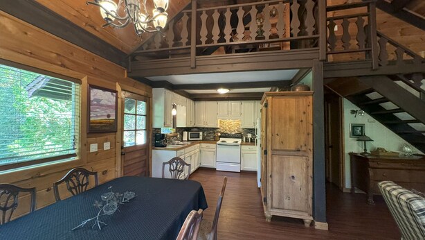 A rustic cabin interior with a dining area, kitchen, and a loft bedroom. - Hummingbird Hideaway - Lake Pets Hike Fish (Almond)