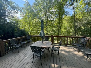A wooden deck with a table and chairs, surrounded by trees. - Hummingbird Hideaway - Lake Pets Hike Fish (Almond)
