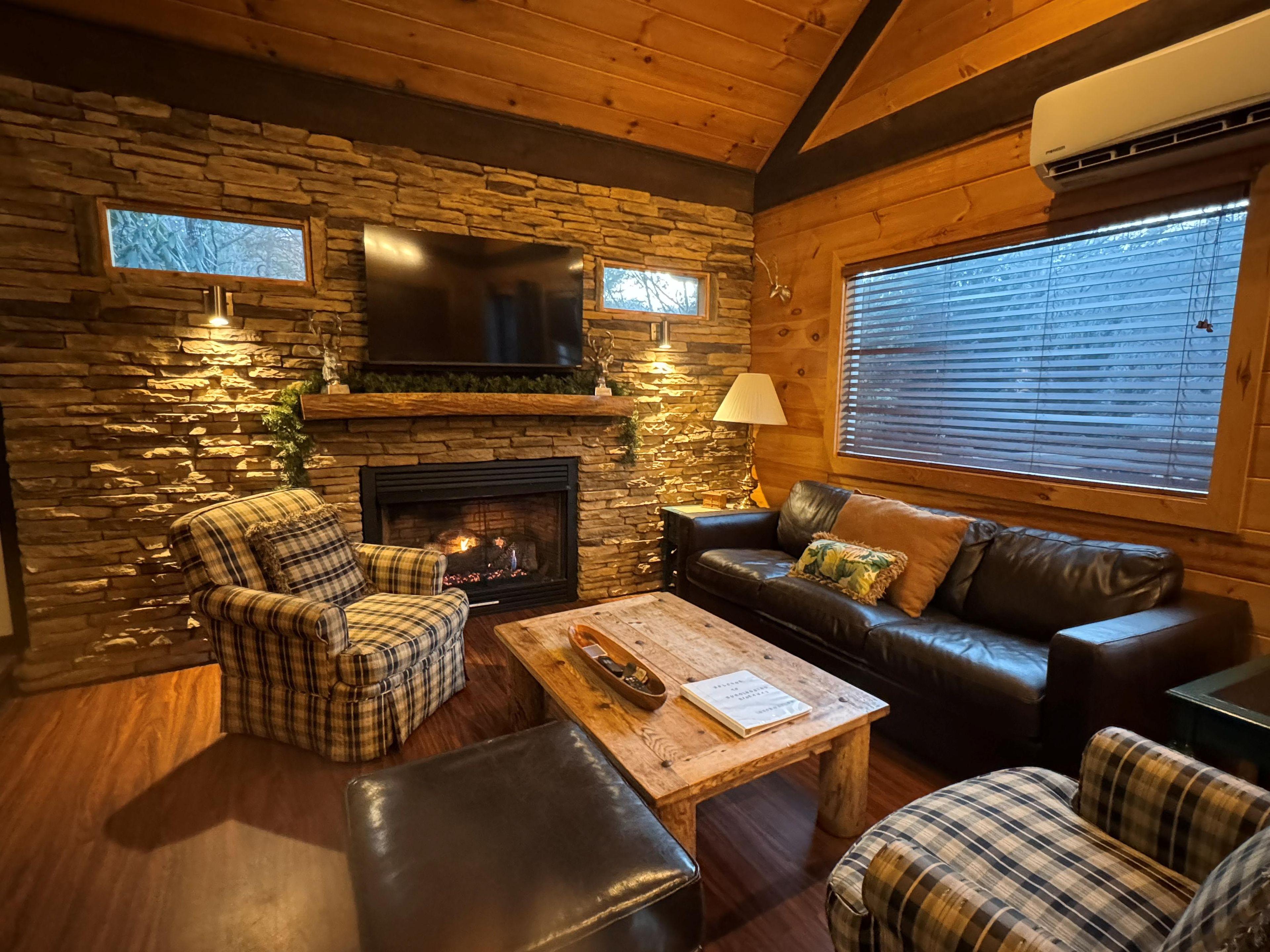 A cozy living room with a stone fireplace, leather sofas, and a television mounted on the wall.