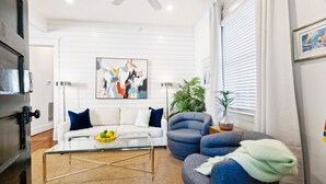 A modern living room with a white sofa, a blue armchair, a glass coffee table, and a painting on the wall. - A2 at Saint Philip Square, One Block to King, Stylish Southern Escape (Charleston)