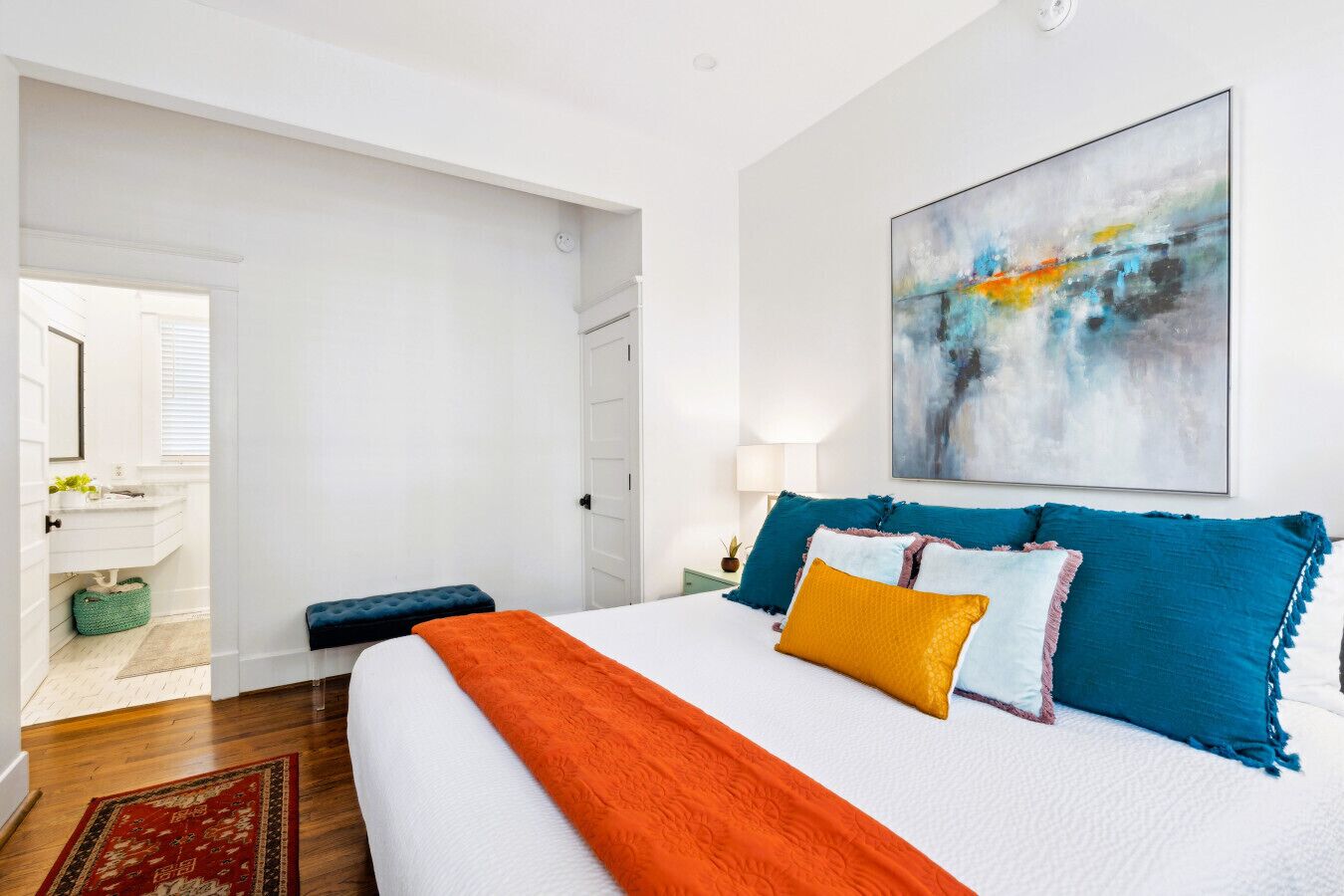 A modern bedroom with a large bed, a painting, and a view to the bathroom.