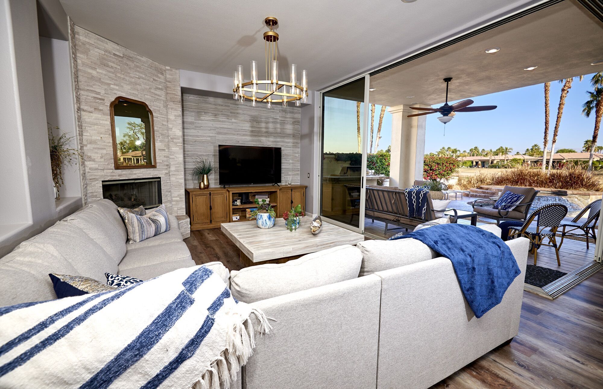 A modern living room with a stone fireplace, a flat-screen TV, and a large window overlooking a pool area.