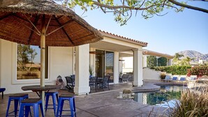 Une terrasse couverte avec des sièges d’extérieur, une piscine et une vue sur les montagnes.