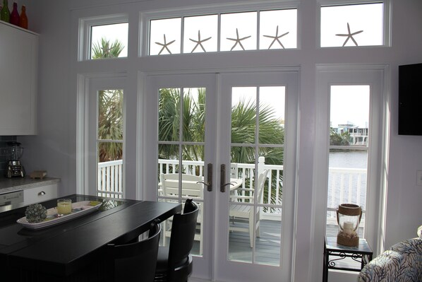 A kitchen with a dining area, a view of the deck and water, and a TV mounted on the wall.