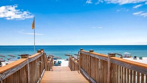 Une terrasse en bois menant à une plage agrémentée de parasols et de chaises longues.