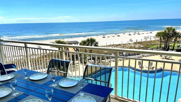 Une table à manger dressée pour six personnes, avec vue sur une plage et une piscine.