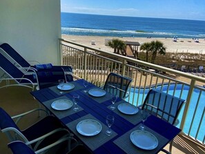 Een balkon met een tafel voor vier personen, met uitzicht op een strand en een zwembad.