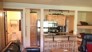 A compact living space with a kitchenette, a dining area with stools, and a seating area with a sofa and a table.