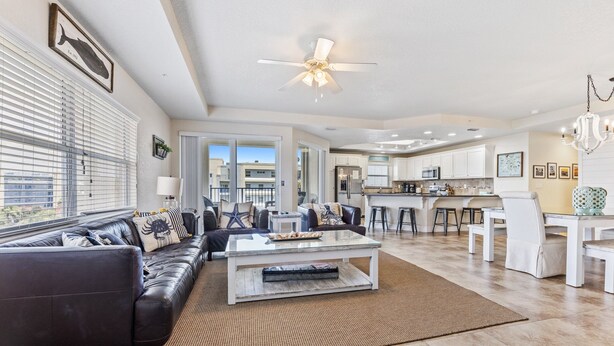 A spacious living room with a dark leather sofa, a glass coffee table, and a view of the kitchen and dining area.