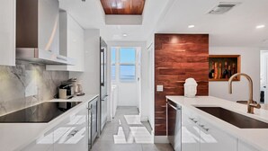 A modern kitchen with white cabinetry, a wooden accent wall, and a view to the outside. - 2/2 Beachfront, VIEWS, Pool, Private Beach Access (Longboat Key)