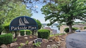 A sign for Parkside Place with a sailboat graphic, surrounded by greenery and a view of a lake and houses.