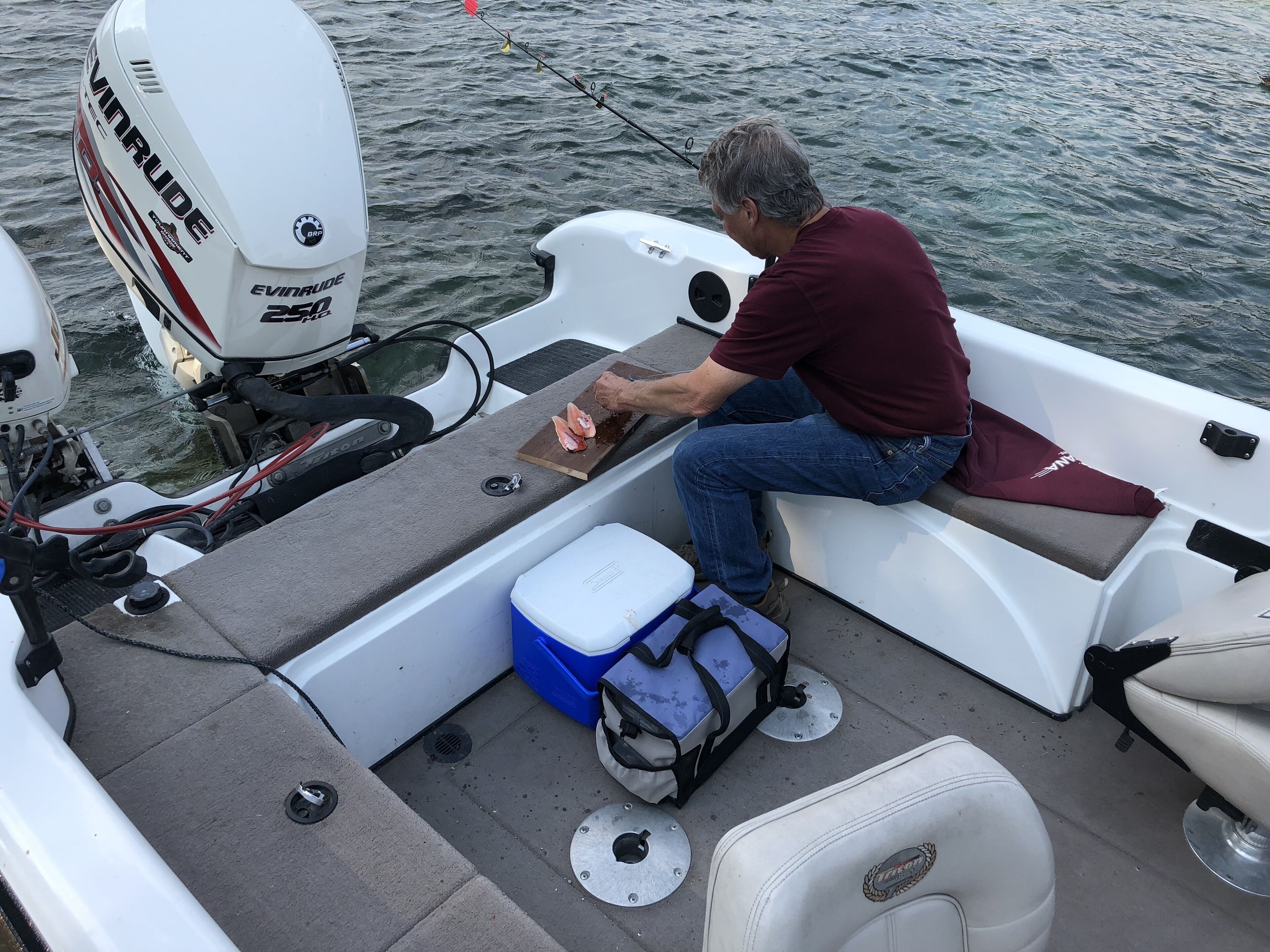 A boat interior with a seating area, a cooler, and a fishing rod.