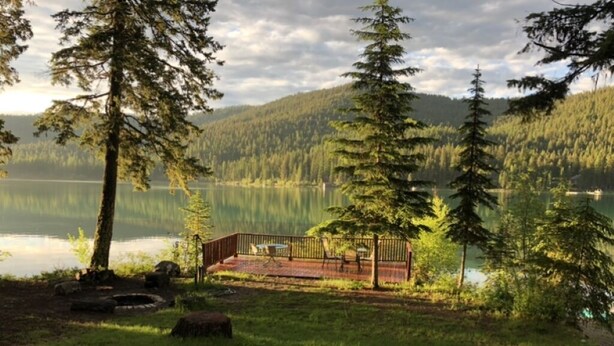Terraza frente al lago con barandilla de madera, rodeada de árboles y vistas al lago y colinas boscosas.