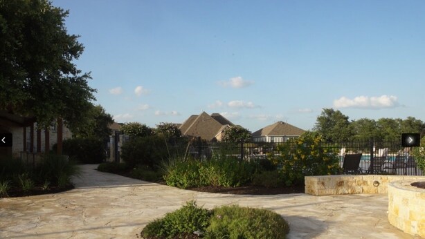 A paved courtyard with a central garden, a pool area with lounge chairs, and a gated entrance with a fence. - The Place to Relax in San Antonio, only 10 min away from Six Flags Fiesta Texas! (San Antonio)