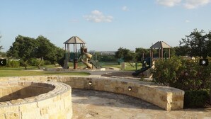 A playground with slides and climbing structures, surrounded by a stone wall and greenery. - The Place to Relax in San Antonio, only 10 min away from Six Flags Fiesta Texas! (San Antonio)