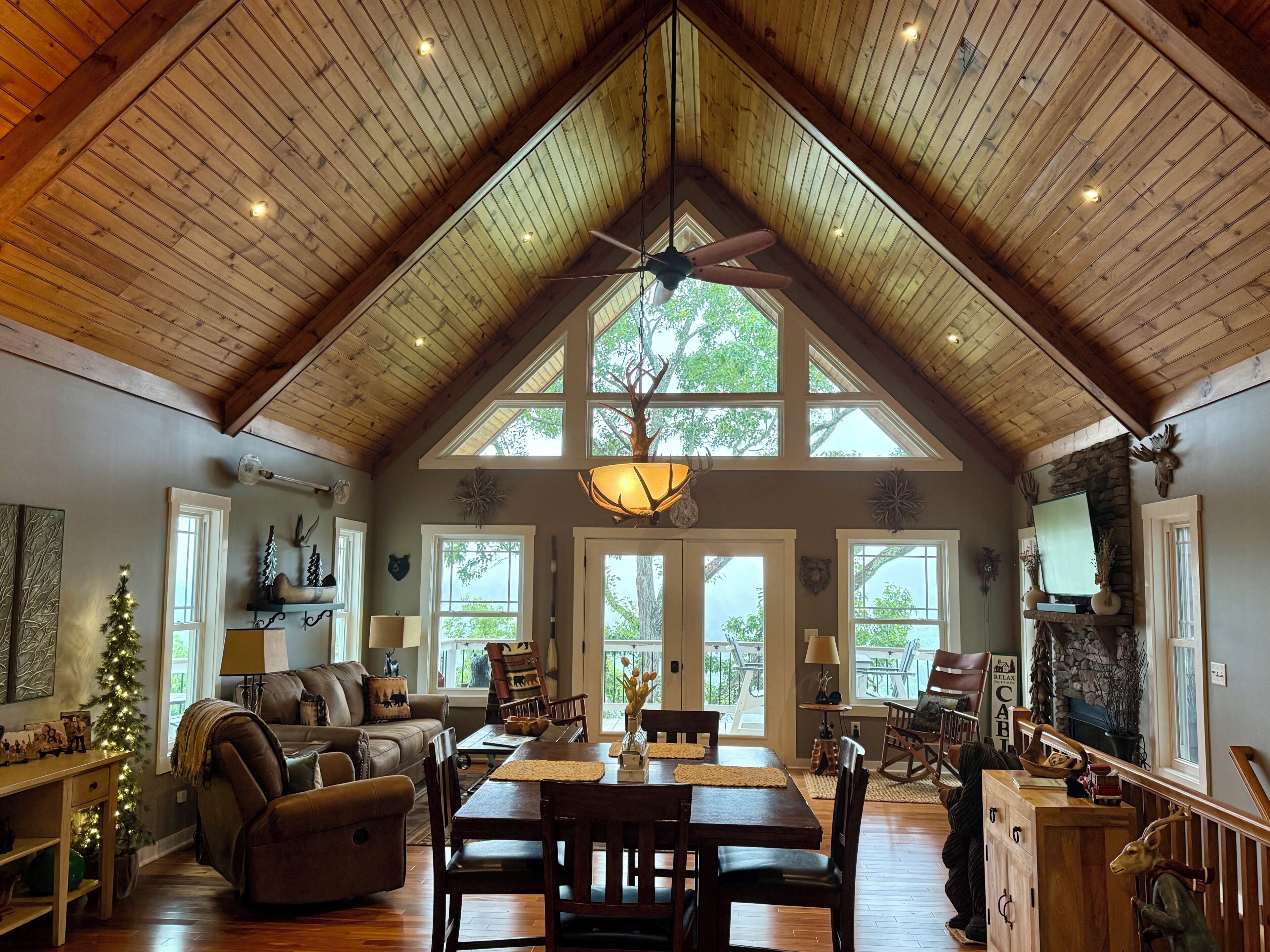 A spacious living area with a high ceiling, wooden beams, a dining table, and a fireplace.