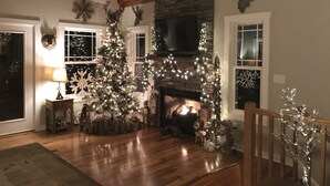 Un salon chaleureux avec un grand sapin de Noël, une cheminée et un plancher en bois.
