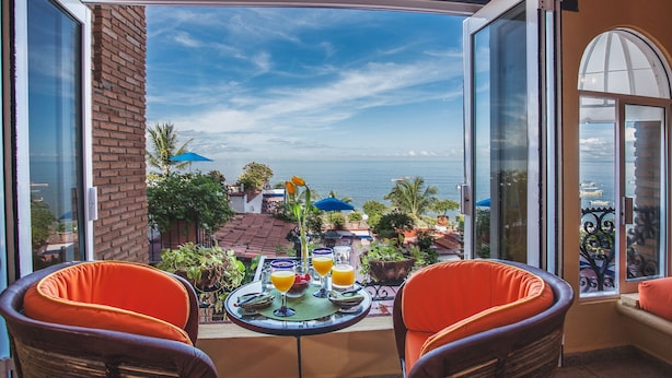 A balcony with two orange chairs, a table with drinks, and a view of the sea. - On Los Muertos beach (Puerto Vallarta)