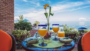 A table with two glasses of orange juice, a vase with flowers, and a view of the sea and boats. - On Los Muertos beach (Puerto Vallarta)