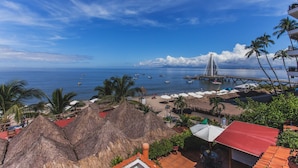 A coastal view with a bridge, beach umbrellas, and thatched-roof huts. - On Los Muertos beach (Puerto Vallarta)