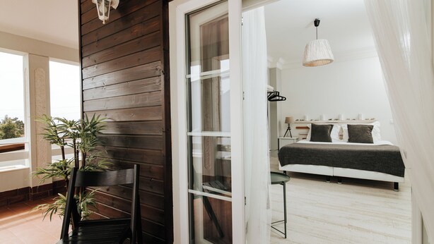 A bedroom with a bed, a bedside table, a hanging light fixture, and a window with curtains.