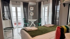 A hotel room with a bed, a desk, two chairs, a TV, and a window with curtains.