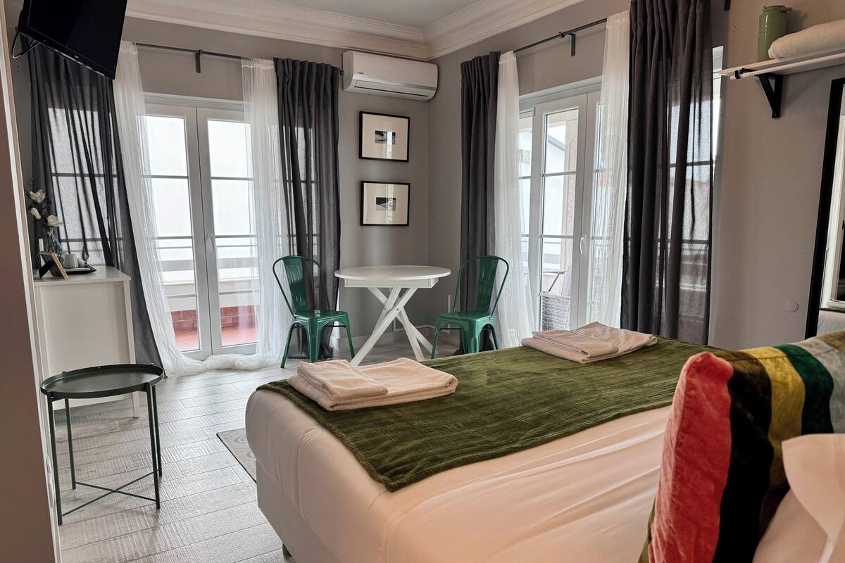Una camera d'albergo con un letto, una scrivania, due sedie, una televisione e una finestra con tende.
