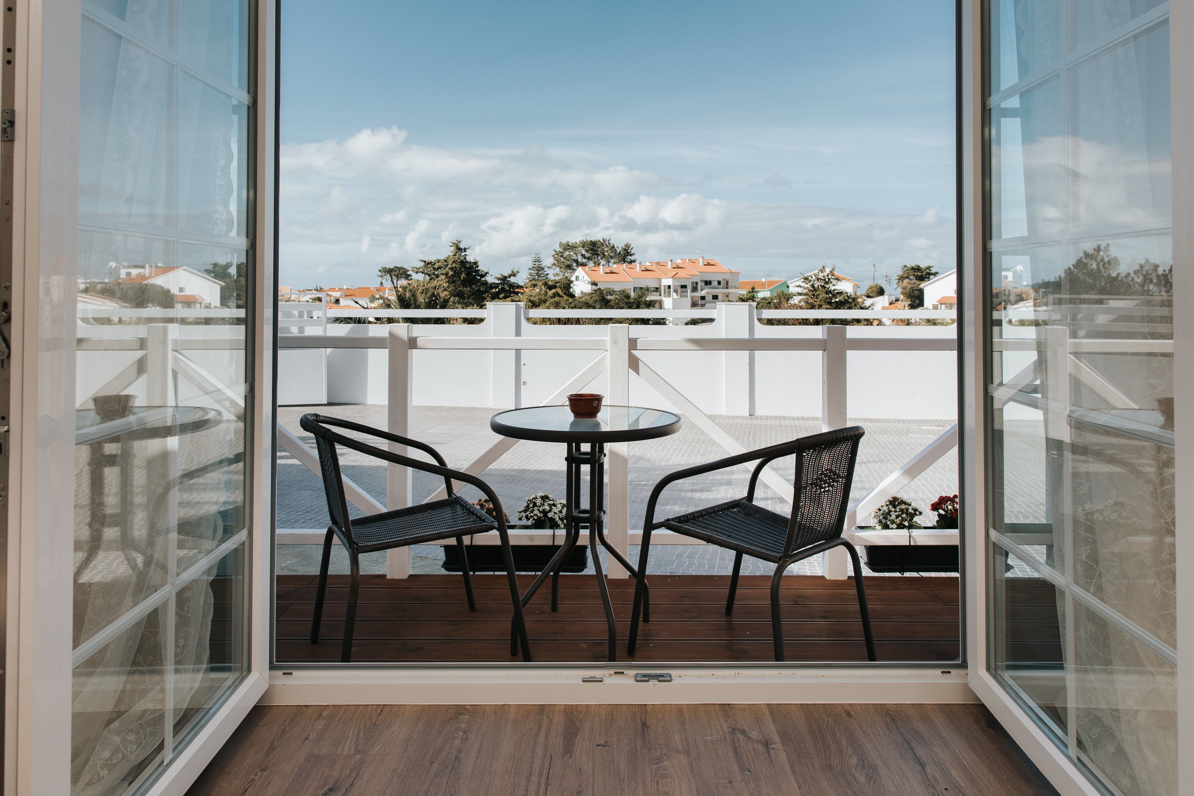 A balcony with two chairs and a small table, overlooking a residential area with houses and trees.