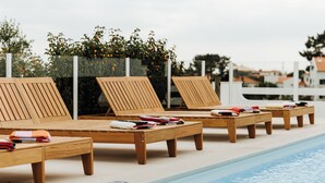A poolside area with wooden lounge chairs and benches, some with towels and swimwear.