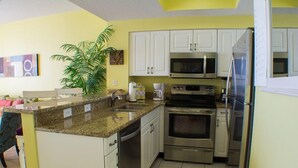 A compact kitchen with white cabinets, stainless steel appliances, and a granite countertop.