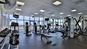 A gym with various exercise equipment, large windows, and a view of the outside.