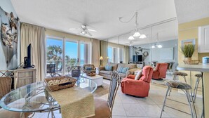 A spacious living area with a balcony, a dining table, and a kitchen area.