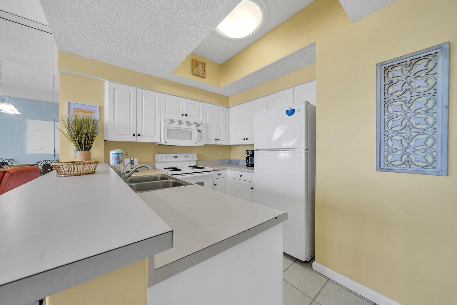 A modern kitchen with white cabinets, a microwave, stove, and refrigerator. There is a sink and a decorative plant on the counter.